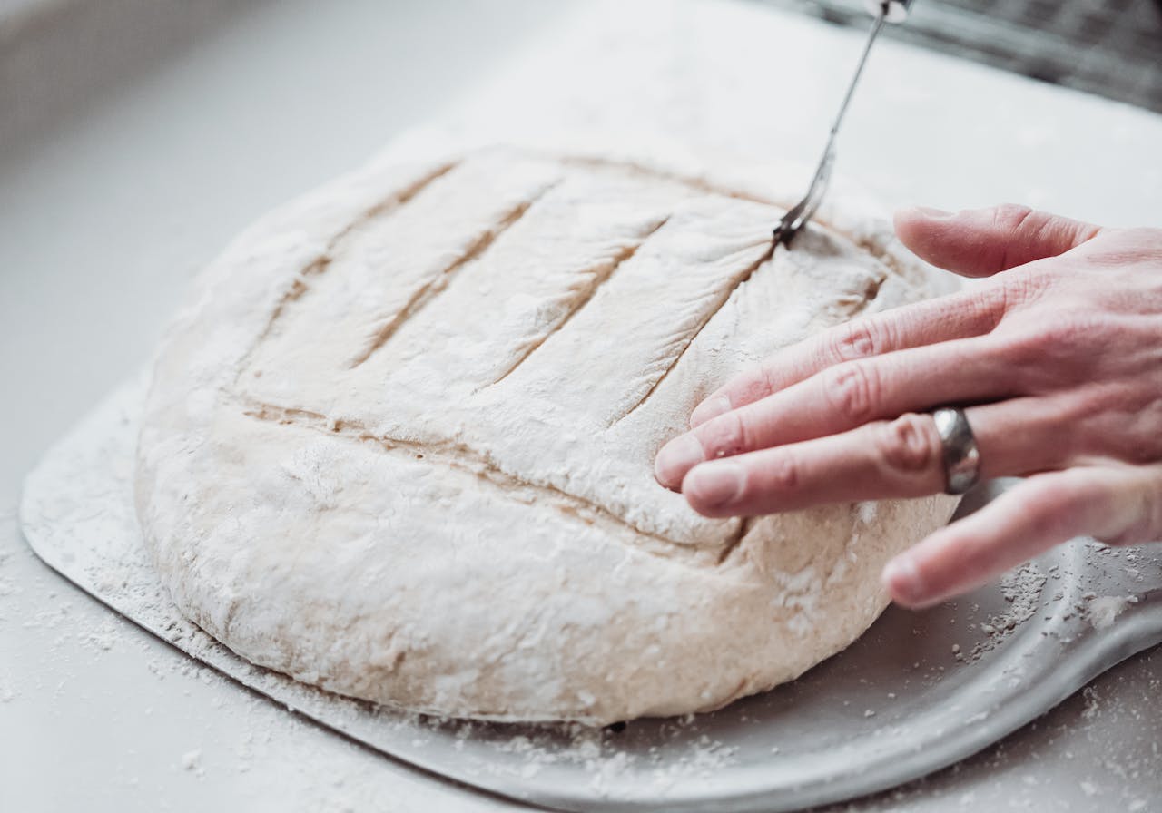 <p> Scoring, or making shallow slashes in the dough, serves both a functional and decorative purpose. Functionally, it allows the dough to expand and rise evenly during baking, preventing it from cracking in undesirable places. A sharp knife or bread lame is ideal for this task. Decorative scoring patterns, like a simple cross or intricate leaf shapes, can also enhance the visual appeal of your bread. Just be sure to score your dough gently—pressing too hard could deflate it. </p> :: Pexels
